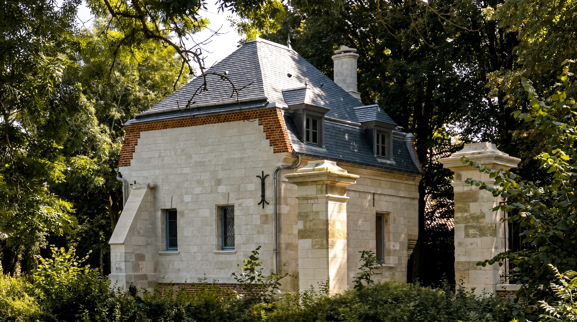 Pavillon en pierre de taille calcaire à joints fins, toit en pavillon couvert d'ardoise naturelle bleue, lucarne à fenêtre à meneaux