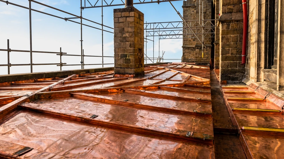 Vue depuis le faîtage d'une toiture en cours de réfection, tuiles plates terre cuite neuves posées en recouvrement, échafaudages métalliques tubulaires sur les côtés