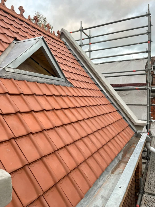 Ouvrier en combinaison de protection intégrale blanche travaillant sur toiture en ardoises, utilisant une échelle aluminium pour accéder aux tuiles défaillantes