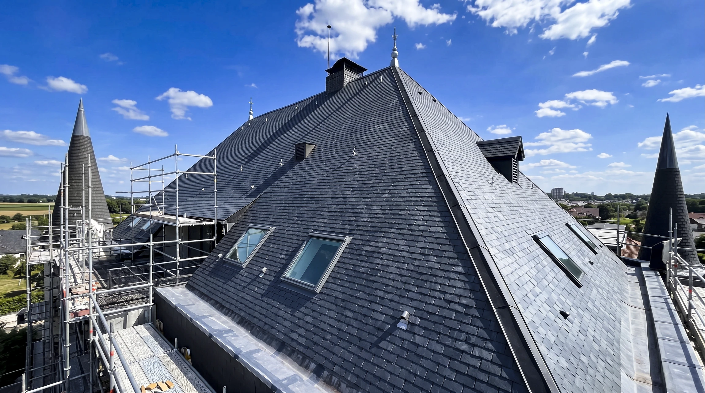 Ouvrier en combinaison de protection intégrale blanche travaillant sur toiture en ardoises, utilisant une échelle aluminium pour accéder aux tuiles défaillantes
